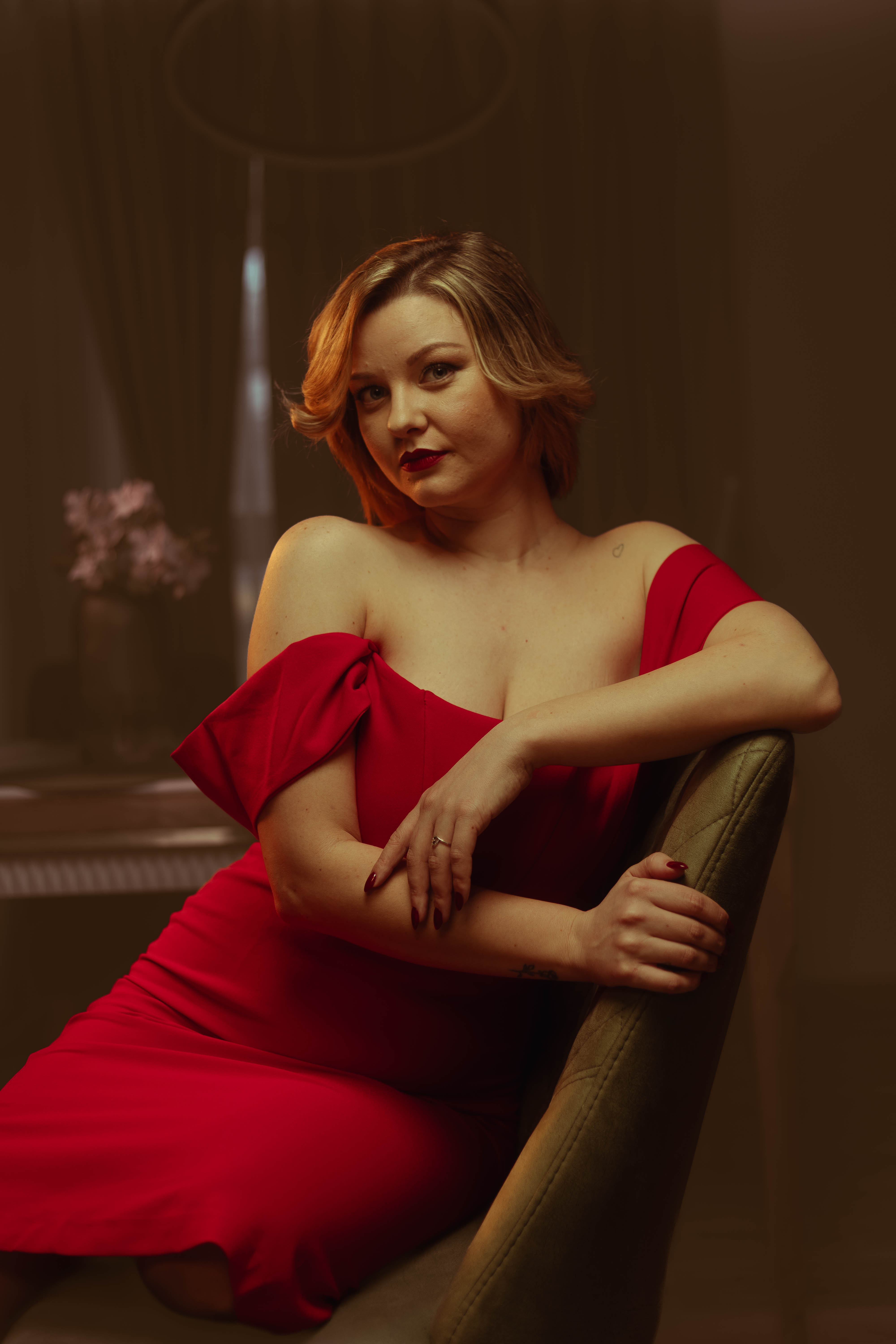Vintage editorial, crimson dress, warm tungsten window light, painterly seated pose
